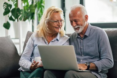 Happy senior couple enjoying while surfing the net together on laptop in the living room. 