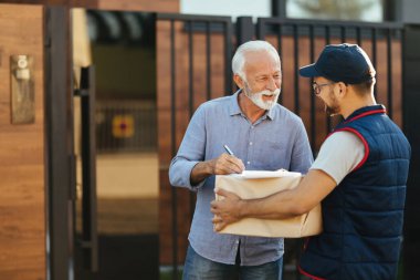 Happy senior man talking to a courier while getting his package delivered at home. 