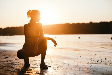 Young sportswoman crouching by the river and enjoying in the morning sun. Copy space. 