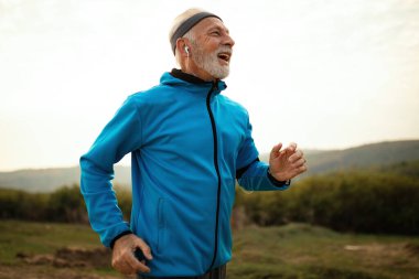 Happy mature athletic man feeling motivated while running in the morning in nature