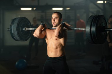 Muscular build man lifting barbell on strength training in a gym.