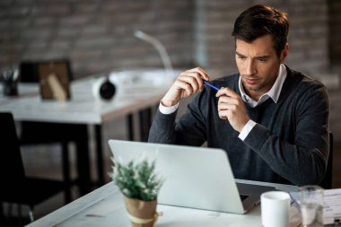 Mid adult entrepreneur working on laptop and reading an e-mail in the office. 