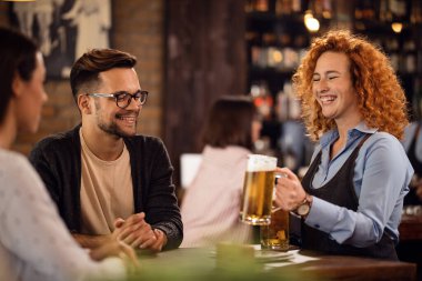 Young cheerful waitress bringing beer to her guests in a bar. 