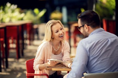 Cheerful woman having fun while using digital tablet with her boyfriend and talking to him in a cafe. 