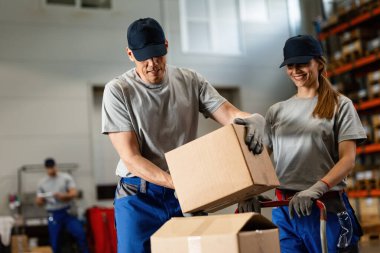 Two smiling workers loading packages and cooperating in distribution warehouse. 
