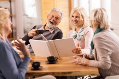 Group of mature friends talking and having fun while remembering their old times by looking at photo album at home. 
