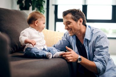 Cute baby boy sitting on the sofa while father is touching his foot. 