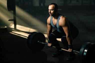 Young sportsman having weight training with barbell in health club. 