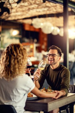 Young couple drinking wine and having fun during lunch in a bar. Focus is on man. 