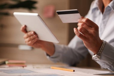 Unrecognizable businesswoman using credit card and digital tablet while e-banking at her office. 