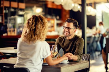 Happy man communicating enjoying with his girlfriend while holding her hand and drinking wine in a restaurant. 