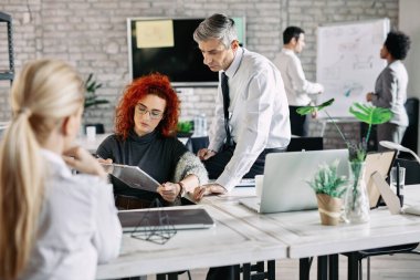 Young businesswoman and her male colleague talking while planning business strategy on a meeting. There are people in the background. 