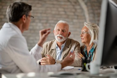 Senior couple communicating with a  doctor about their healthcare insurance plans at clinic. 