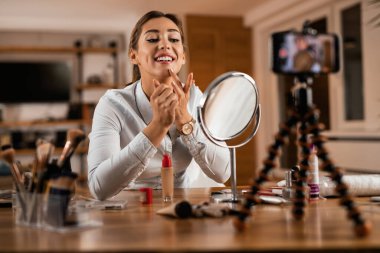 Young female influencer applying face powder while vlogging at home. 