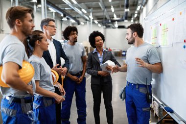 Young factory worker holding presentation about production development to company managers and his coworkers. 
