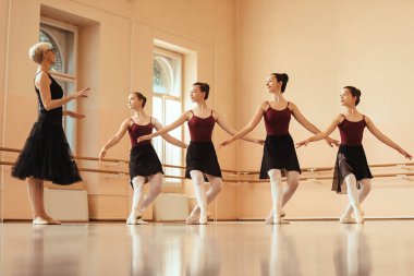 Mature ballet instructor teaching group of ballerinas at dance studio.