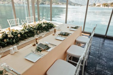 Decorated table setting in weeding reception hall with view at the sea through the windows. 
