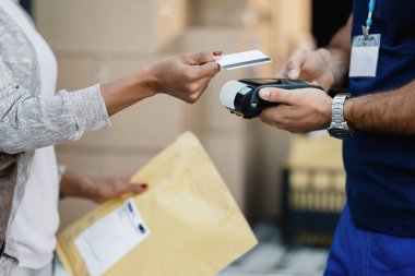 Close-up of African American woman making contactless payment to a courier for package delivery. 