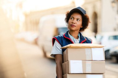 Black female deliverer carrying packages while walking in the city. 