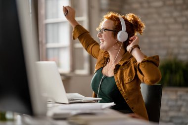 Happy creative woman enjoying in her favorite song while working on laptop in the office. 