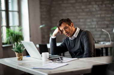 Overworked businessman sitting at his desk and thinking of something in the office. 