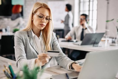 Serious businesswoman making payments online with a credit card while sitting at her desk in the office. 