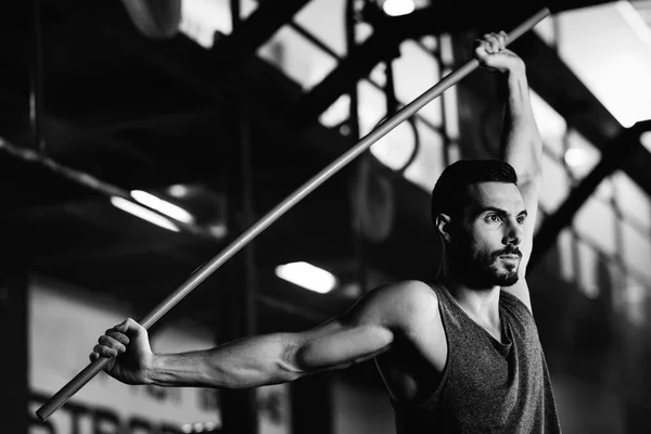 Black and white photo of athletic man exercising with weight bar on cross training in health club.