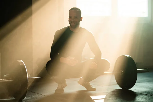 Young happy athletic man lifting weights on cross training in a gym.