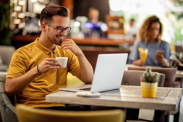 Happy man relaxing in a cafe and surfing the net on a computer while drinking coffee.