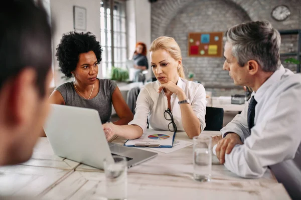 Mid Adult Businesswoman Talking Her Colleagues While Using Laptop Pointing — Fotografia de Stock