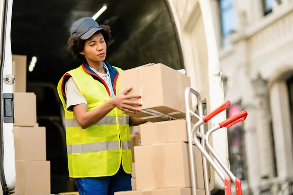 Black female deliverer unloading packages from a van in the city.