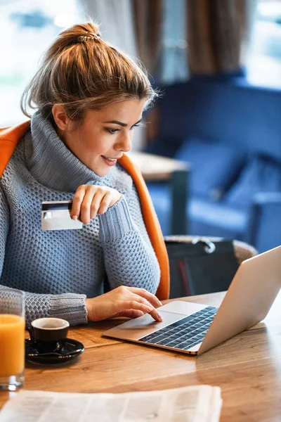 Young businesswoman relaxing on coffee break and using credit card and laptop for online shopping.