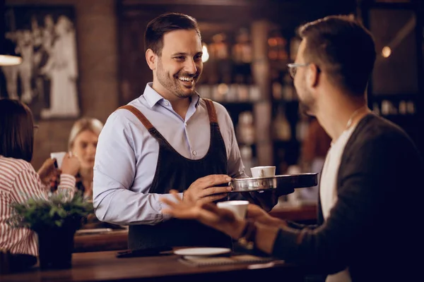 Young Happy Waiter Talking His Customer While Serving Him Coffee — Fotografia de Stock