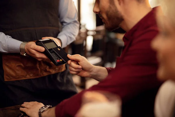 Close up of man using credit card while making contactless payment in a cafe.