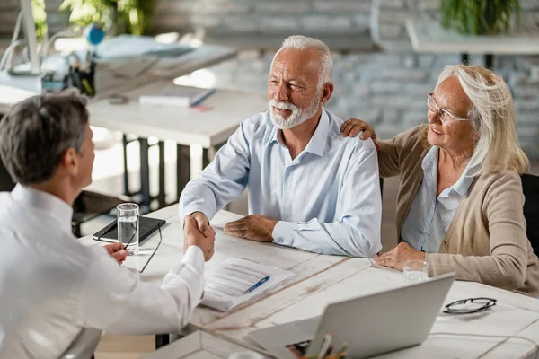 Happy senior couple shaking hands with insurance agent after successful agreement on a meeting in the office. 