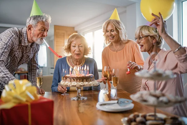 Счастливая Пожилая Женщина Задувает Свечи Торте Празднуя День Рождения Дома — стоковое фото