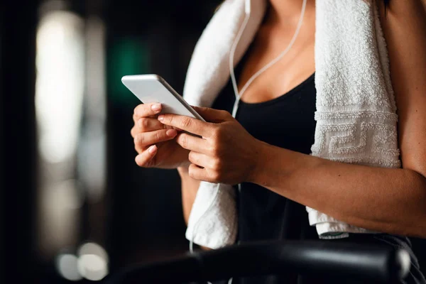 Unrecognizable sportswoman text messaging on smart phone while exercising in a gym