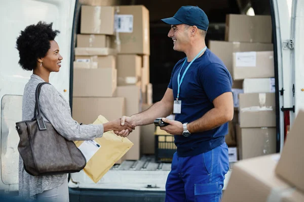 Happy African American woman shaking hands with a courier while getting her package delivered. Focus is on man.