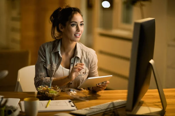 Female freelancer using touchpad while reading e-mail on desktop PC at night at home.