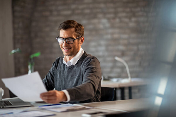 Smiling entrepreneur working on business reports while sitting at his office desk. 