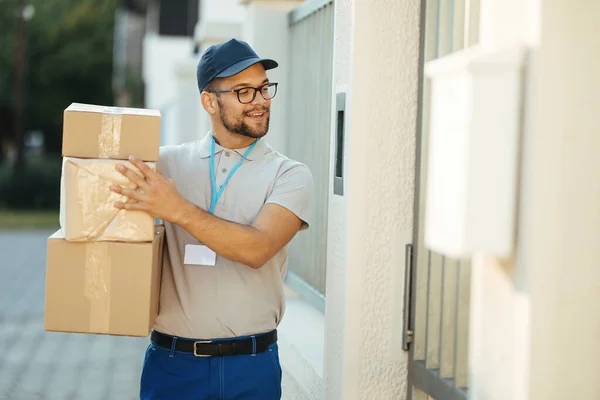 Happy courier with packages talking on intercom while making home delivery.