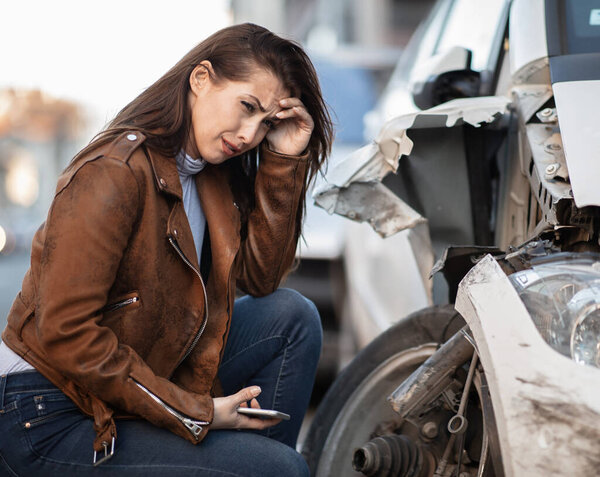Young woman in despair crying next to her wrecked car.