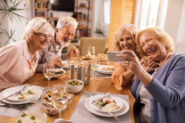 Group of carefree senior friends having fun while taking selfie during lunch time at home.