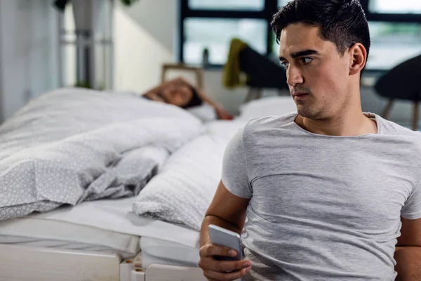 Pensive Man Using Mobile Phone Cheating His Girlfriend Who Sleeping — Stockfoto