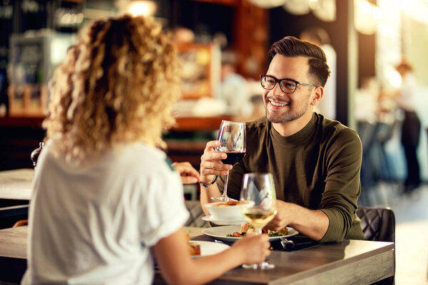 Young happy man talking to his girlfriend while drinking wine and eating in a restaurant. 