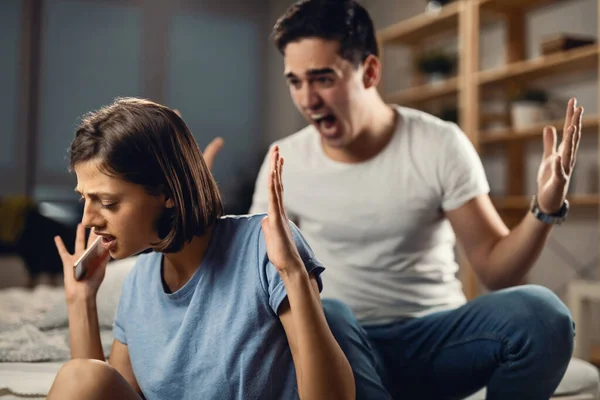 Young couple arguing in the bedroom. Young woman is trying to ignore her angry boyfriend while he is yelling at her.