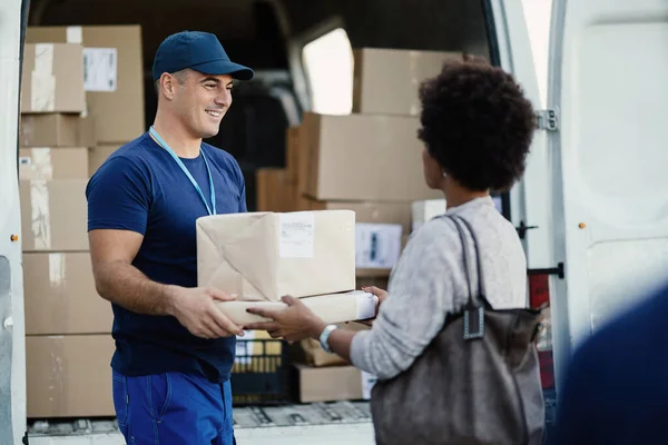 Happy courier making a delivery and giving packages to African American woman.