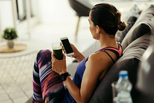 Sportswoman Using Mobile Phone Drinking Detox Smoothie Sofa Home —  Fotos de Stock