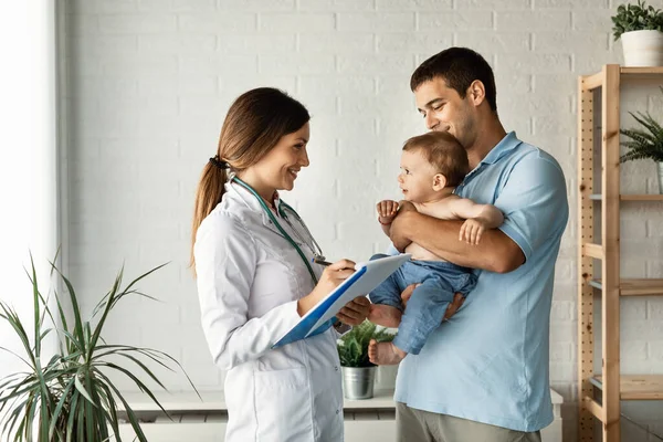 Happy Female Pediatrician Writing Medical Report While Talking Small Boy —  Fotos de Stock