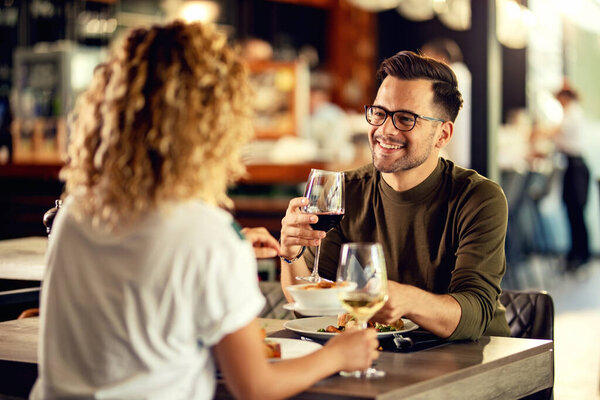 Young happy man talking to his girlfriend while drinking wine and eating in a restaurant. 